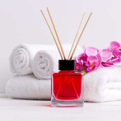 A red bottle with a four wick diffusers sits on a white table